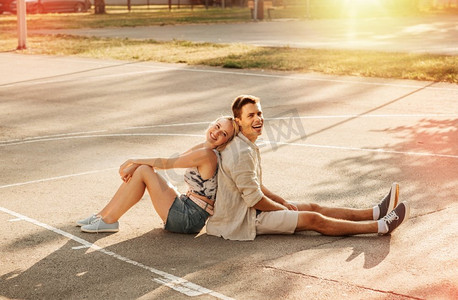 暑假和人们的概念—快乐的年轻夫妇背靠背坐在篮球场上。快乐的夫妇坐在篮球场
