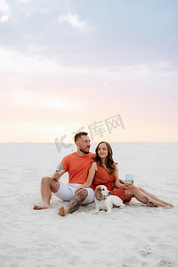 穿着橙色衣服的年轻夫妇带着狗在沙漠中的白沙
