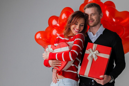 快乐的微笑夫妇与红心形状气球和礼物，情人节。夫妇与心气球和礼物