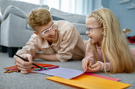 铅笔画铅笔摄影照片_在家里的地板上用铅笔画出幸福的父女俩的小孩子。父女俩在地板上作画