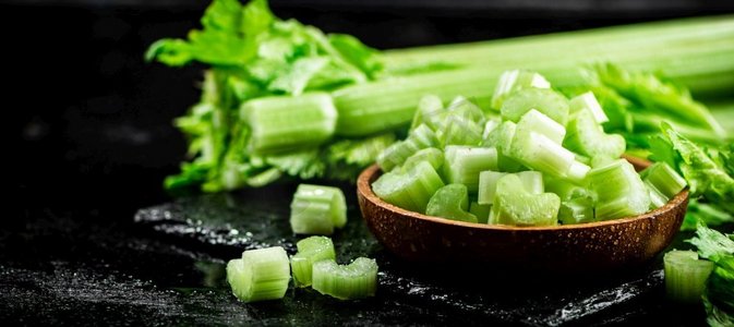 新鲜的绿色蔬菜摄影照片_一片新鲜的芹菜放在一个木盘子里。黑色背景。高质量的照片。一片新鲜的芹菜放在一个木盘子里。 