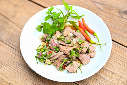 辛辣的肝沙拉在白色板木桌子背景，与新鲜的辣椒香草，香料，泰国食物的猪肝沙拉 