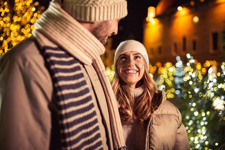 寒假和人们概念快乐的夫妇在晚间的圣诞树彩灯下微笑。圣诞彩灯下幸福的夫妇微笑着