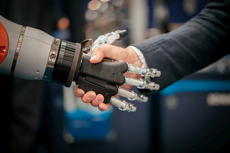 握手交互合作摄影照片_一个商人与Android机器人握手的手。人类与人工智能交互的概念。