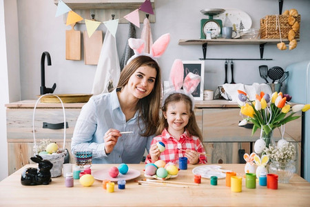 复活节恐龙彩蛋摄影照片_可爱的小女孩兔耳朵和妈妈一起画复活节彩蛋