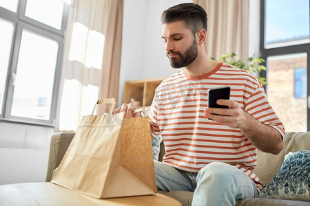 沟通、休闲和人际概念—男子在家中使用智能手机进行外卖订购检查。一名男子用电话检查家中的食品订单