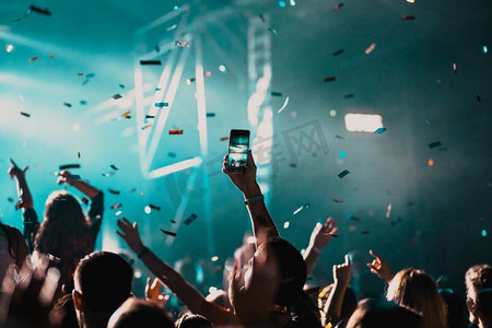 五彩摄影照片_音乐会音乐节上举起手和掉落的五彩纸屑欢呼的人群