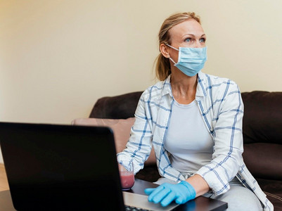 隔离感染摄影照片_隔离期间戴医用口罩在家工作笔记本电脑的妇女