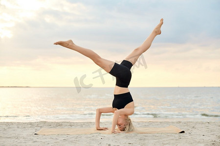 健身，运动，和健康的生活方式概念—妇女做瑜伽头倒立在海滩超过日落。妇女做瑜伽倒立在海滩