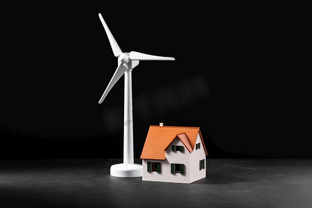 能源，电力和可持续性概念—风力涡轮机和房子模型特写镜头在黑色背景。风力涡轮机和房屋模型特写