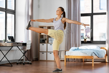 运动，健身和健康的生活方式概念—微笑的少女在家里锻炼和伸展腿。快乐的十几岁的女孩锻炼在家里