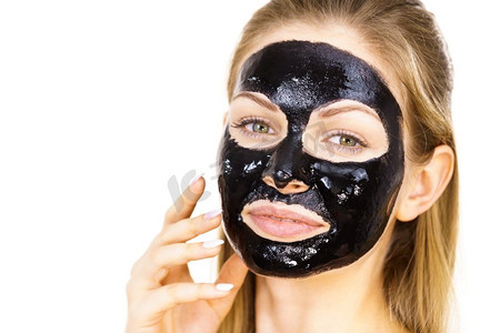 对面膜摄影照片_年轻女子与化妆品在脸上，碳水化合物排毒黑色剥离面膜。水疗护理。护肤品妇女与黑色剥离关闭面具在脸上