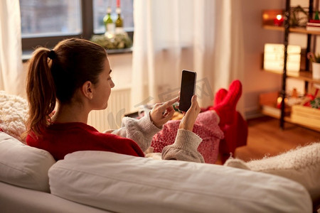 圣诞节标题框摄影照片_圣诞节，冬季假期和休闲概念—年轻妇女使用智能手机在舒适的家。妇女使用智能手机在家里圣诞节