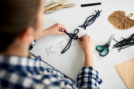 创意绳索摄影照片_DIY，手工和爱好概念-女人在家里的桌子上制作马克龙工艺品和打结绳索的特写。做松糕和打结绳索的女人