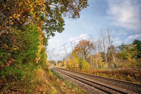 橙色风景摄影照片_铁路通过秋天彩色风景与五颜六色的树在秋天