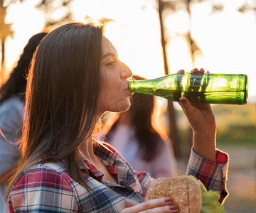 户外喝啤酒摄影照片_边看边和朋友在户外喝啤酒的女人