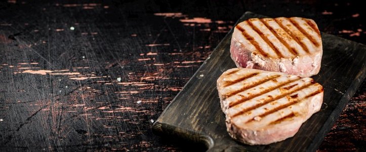 美味的烤金枪鱼牛排放在切菜板上。在质朴的黑暗背景上。高质量的照片。美味的烤金枪鱼牛排放在切菜板上。