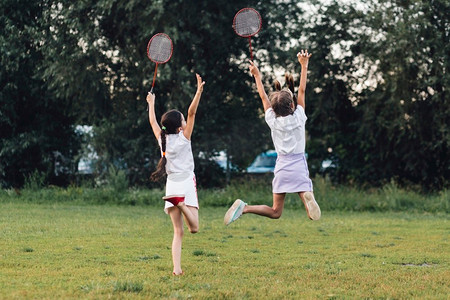 羽毛球框摄影照片_后视图两个女孩跳跃公园举行羽毛球