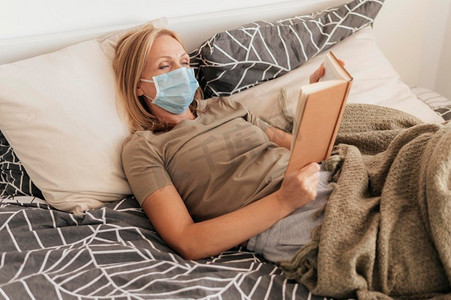 隔离感染摄影照片_戴医用口罩的妇女在家中读隔离读物