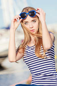 夏天和人们的概念时尚可爱的金发女郎与心形太阳镜在码头反对游艇在港口