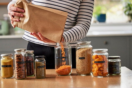 妇女通过填充密封罐储存干燥食品在家里节省包装