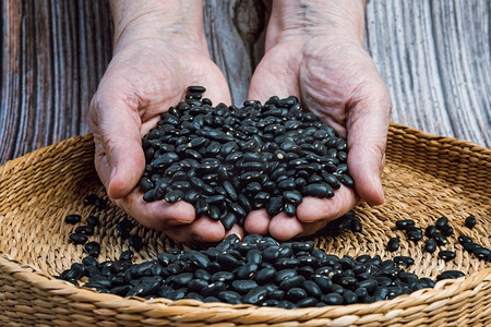 黑色的手摄影照片_棕色的碗里装满了干黑豆。手满是新鲜的黑豆。健康饮食和素食理念。