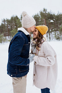 人，爱和休闲概念—快乐的男人亲吻女人额头在冬季森林。快乐的男人亲吻女人到前额在冬天
