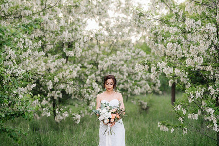 新娘在一个白色礼服与大春天花束在绿色森林