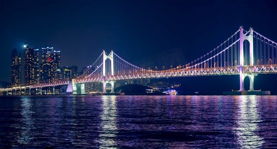 广安桥摄影照片_光岸大桥和摩天大楼在夜色中灯火通明。韩国釜山。光岸大桥和夜间的摩天大楼。韩国釜山