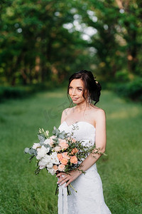 新娘在一个白色礼服与大春天花束在绿色森林
