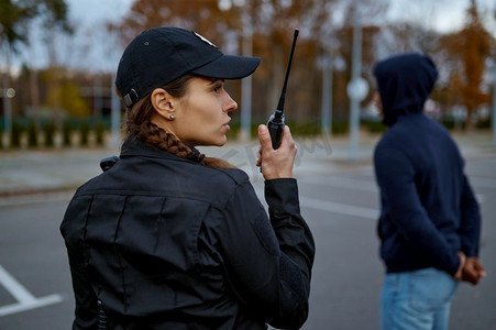 从背面看穿制服的女警察使用便携式无线电为警察通信。女警察使用便携式无线电后视图