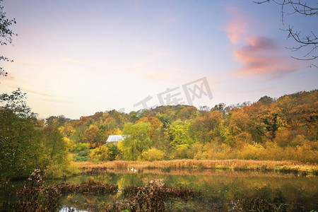 田园诗般的湖在一个森林与一个小小屋由五颜六色的树木包围在秋天