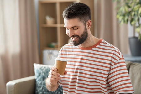 饮料和人的概念—微笑的男人喝外卖咖啡从纸杯在家里。微笑的男人在家里喝外卖咖啡