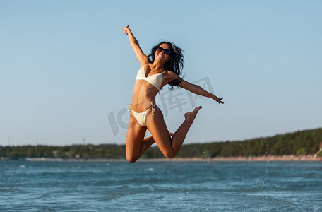 人，夏天和泳装概念—愉快的微笑的年轻妇女比基尼泳装跳跃在海滩微笑的年轻女子比基尼泳装在海滩