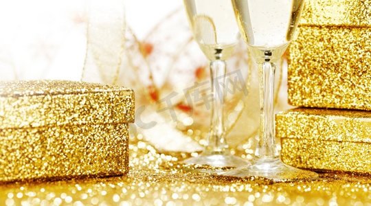 香槟在玻璃杯和礼品盒在金色背景与闪烁的光。香槟和礼品