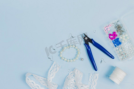 钳子钩珍珠花边丝带线线轴塑料珠盒蓝色背景