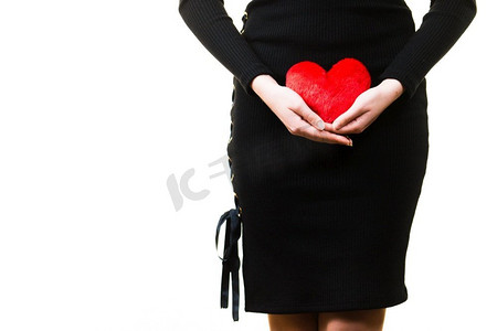 年轻的女人期待着孩子。怀孕的女性拿着小心形枕头在她的肚子。妇女期待婴儿与心脏枕头
