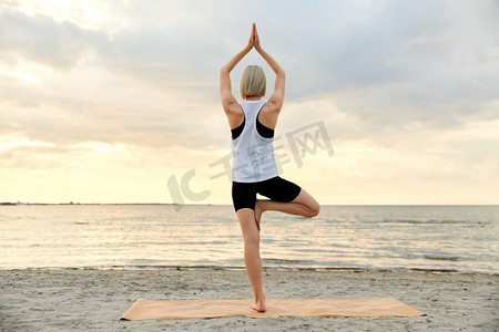 瑜伽大海摄影照片_健身、运动和健康生活方式理念--日落时分，女性在海滩上摆瑜伽树姿势。日落时分，一名女子在海滩上摆瑜伽树姿势