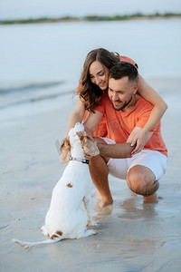 年轻夫妇橙色衣服与狗在空沙滩