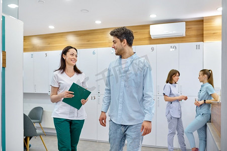 医生和病人会说话和走路。诊所走廊内部，背景是两名护士。医生和病人说话和行走的走廊
