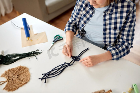 生态家摄影照片_DIY，手工和爱好概念-女人在家里的桌子上制作马克龙工艺品和打结绳索的特写。做松糕和打结绳索的女人