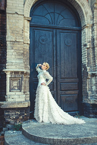 金发女郎在一件复古的衣服在建筑物的旧黑暗门的背景