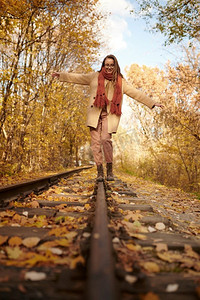 平衡在铁路的年轻浪漫的女人用金叶子覆盖在秋天背景。妇女平衡在铁路在秋天背景