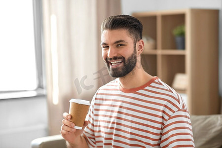 客户家里摄影照片_饮料和人的概念—微笑的男人喝外卖咖啡从纸杯在家里。微笑的男人在家里喝外卖咖啡