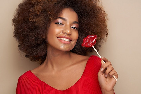 一个非洲女孩的美丽的肖像与嘴唇形状的棒棒糖。情人节。’爱的象征