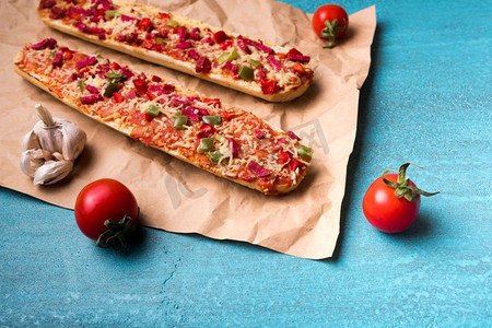美味的法棍披萨樱桃西红柿大蒜棕纸蓝色混凝土背景