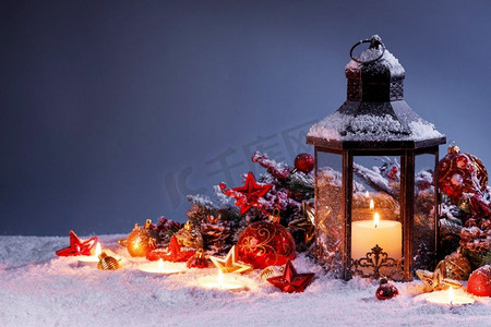 蓝色元宵灯笼摄影照片_燃烧的圣诞灯笼和冷杉装饰在雪在蓝色背景与复制空间。圣诞灯在雪