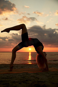 健身、运动和健康的生活方式概念—妇女做瑜伽桥姿势在日落的海滩。妇女做瑜伽桥姿势在海滩