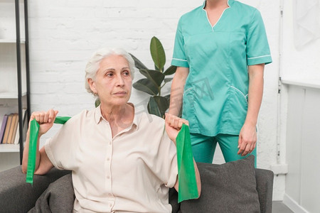 坐在女护士前面的老年妇女带着绿色弹力带锻炼