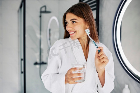 浴室玻璃摄影照片_年轻女子拿着牙刷玻璃水